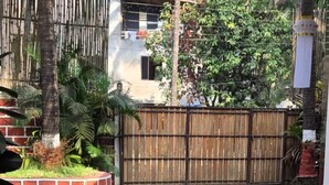 Un patio con un camino de piedra, una gran pila de piedra con flores, una cerca de madera y un edificio al fondo.