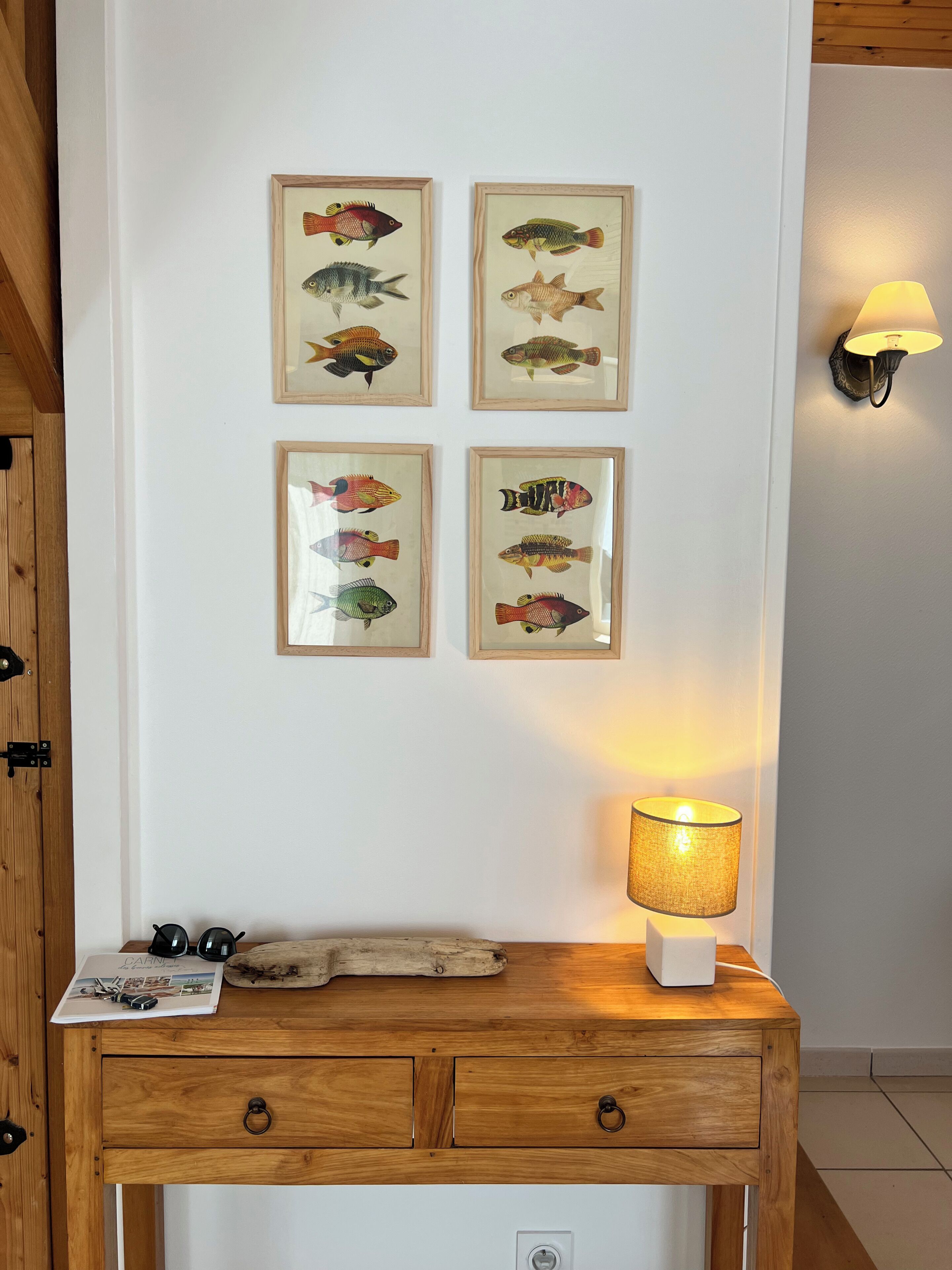 Eine Wand mit vier gerahmten Fischzeichnungen, eine Holzvitrine mit einer Lampe und einer Wandleuchte.