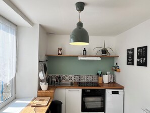 Una cuina moderna amb forn integrat, rentaplats, llum penjant i finestra amb cortines transparents.