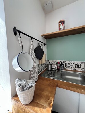Une cuisine avec un étagère à casseroles suspendue, un évier et une petite fenêtre.