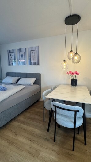 A modern bedroom with a bed, bedside tables, a dining area with chairs, and a wall-mounted light fixture. - Stressless Sky Vacation Apartment, including the Bavarian Forest AktivCard, Sauna, and Pool (Sankt Englmar)