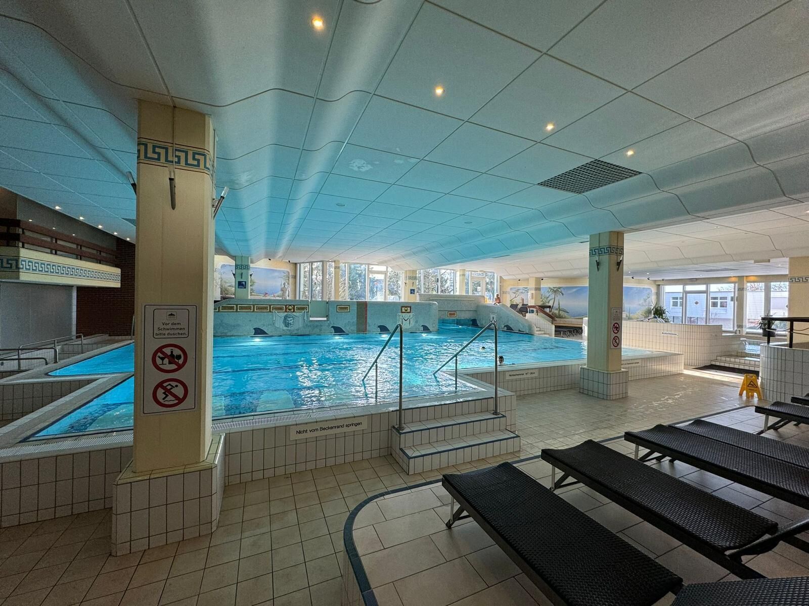 An indoor swimming pool with clear signage, a tiled floor, and a sunlit interior.