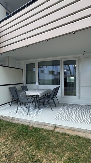 A covered patio with a table and chairs, large windows, and a patterned floor. - Stressless Sky Vacation Apartment, including the Bavarian Forest AktivCard, Sauna, and Pool (Sankt Englmar)