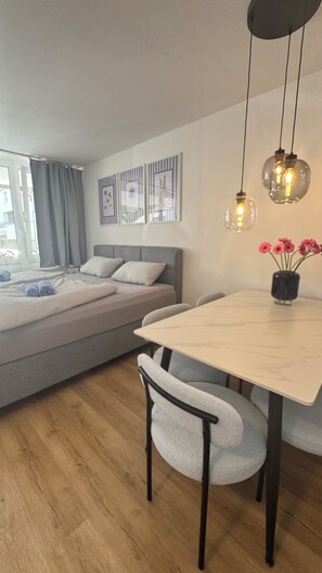 A modern bedroom with a bed, bedside table, and a dining area with a table and chairs. - Stressless Sky Vacation Apartment, including the Bavarian Forest AktivCard, Sauna, and Pool (Sankt Englmar)