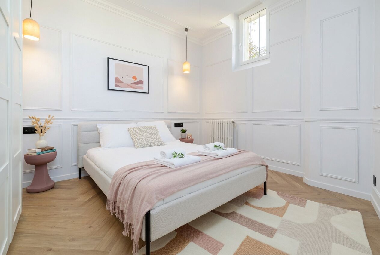 A bedroom with a bed, bedside tables, a radiator, a window, and a wall-mounted picture.