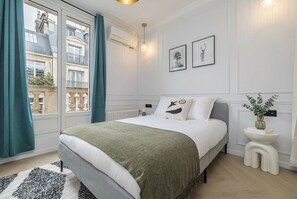 Quarto com cama, janela, radiador e mesa de cabeceira com um vaso.