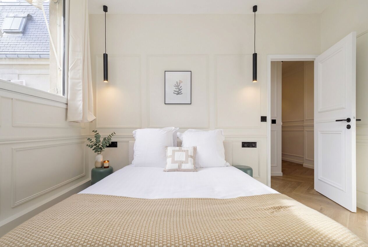 Een slaapkamer met een groot bed, nachtkastjes, een nachtkastje, een ingelijste foto aan de muur en een deur naar een andere kamer.