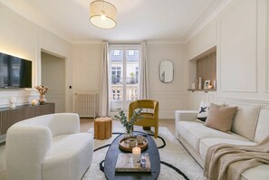 Uma sala de estar moderna com um sofá, poltrona e uma mesa de centro com um livro e uma vela.