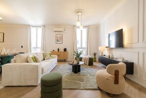 Uma sala de estar moderna com sofá, banquinho, poltrona, mesa de centro e televisão de tela plana fixada na parede.