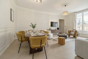 Uma sala de jantar com uma mesa posta para quatro pessoas, rodeada por cadeiras amarelas, um sofá e uma pequena mesa redonda com um abajur.