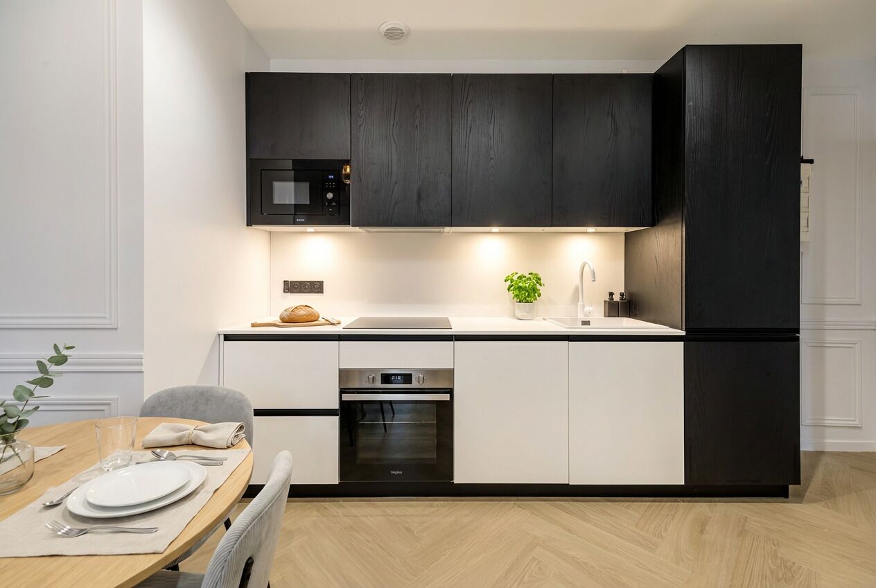 Una cocina moderna con armarios oscuros, microondas empotrado, horno de acero inoxidable y refrigerador.