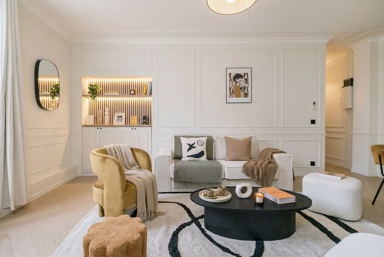 Uma sala de estar moderna com sofá, poltrona, mesa de centro e uma estante decorativa.