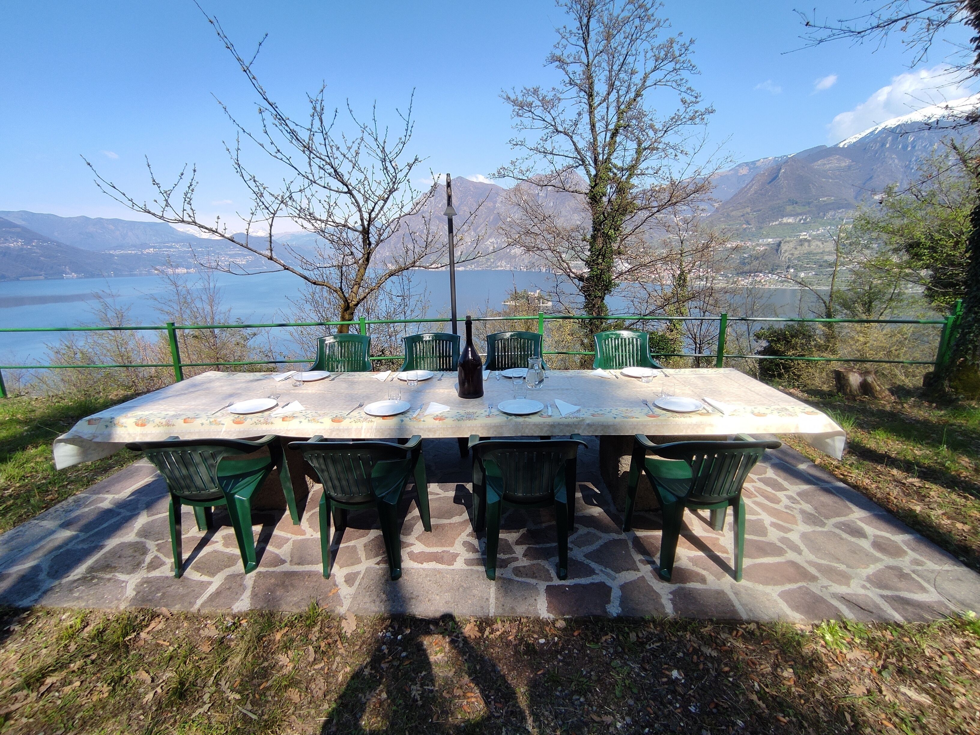 An outdoor dining table with chairs, set on a stone patio with a view of mountains and a lake.