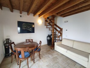 Een eetgedeelte met een houten tafel en stoelen, een bank, een trap en een kunstwerk aan de muur.