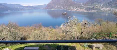 A lakeside view with mountains, a small island, and a dining area with a table and chairs.