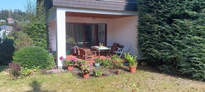 Eine Terrasse mit Gartenmöbeln, einem Glastür-Eingang und Blumentöpfen.