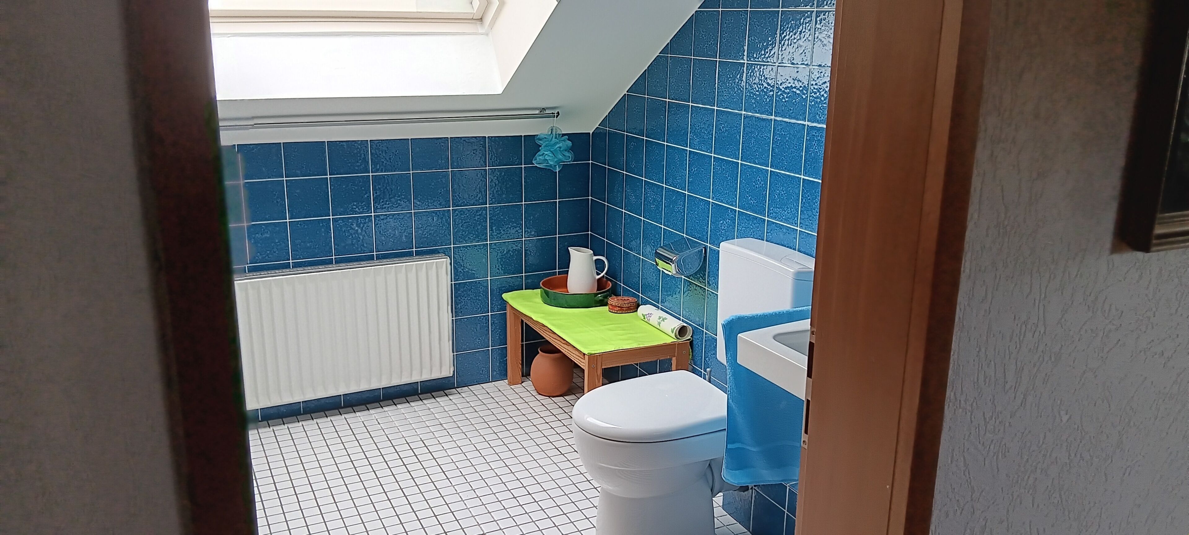 Een kleine badkamer met een dakraam, een toilet, een wastafel en een blauwe betegelde wand.