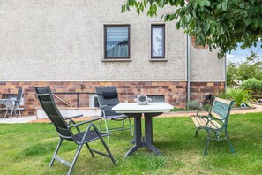 An outdoor seating area with a table and chairs, a bench, and a brick wall with windows.