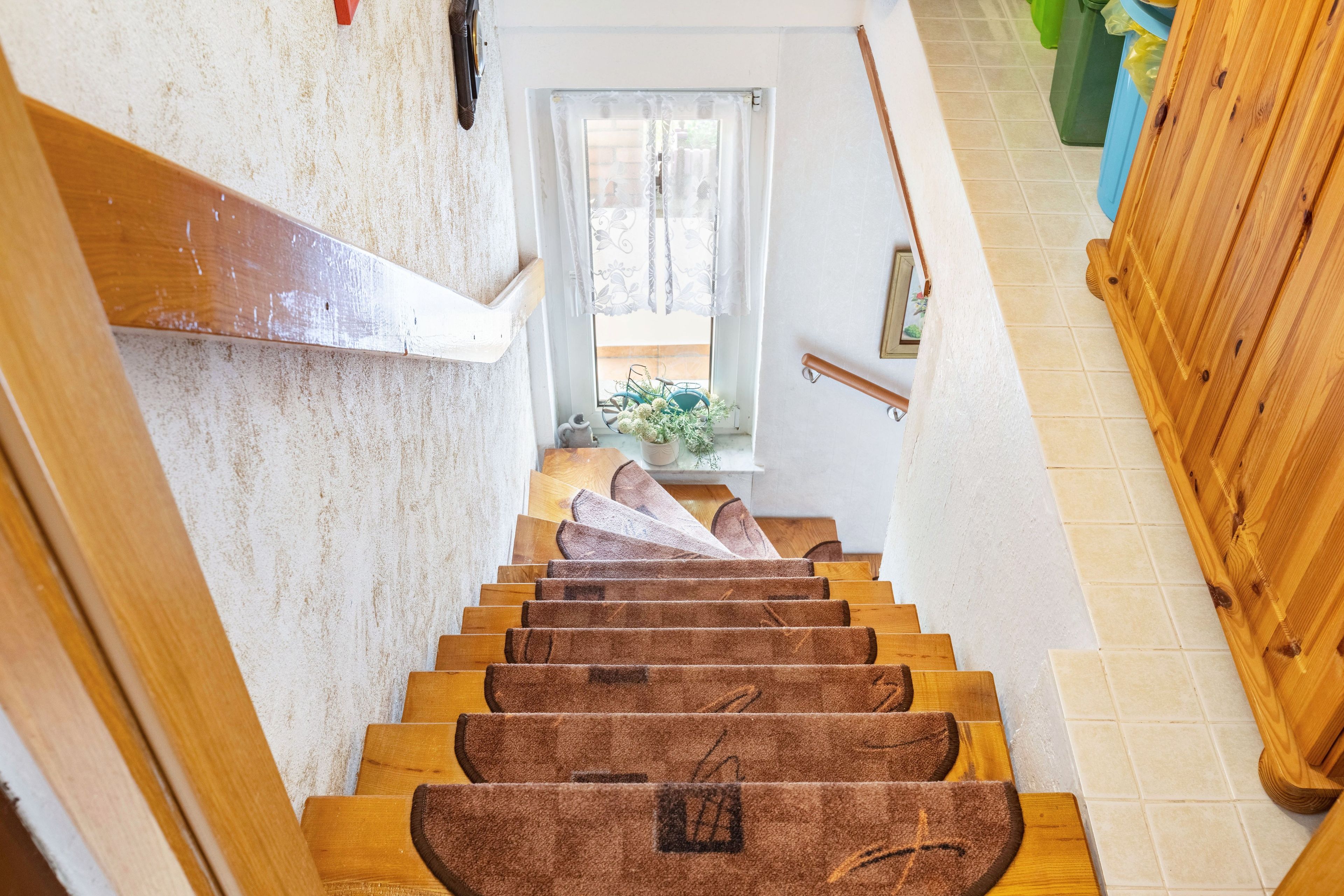 A wooden staircase with a handrail, leading to a room with a window and a door.