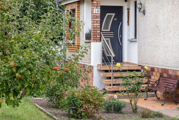 A residential building with a brick facade, a black door, and a small garden with a bench and a rose bush.