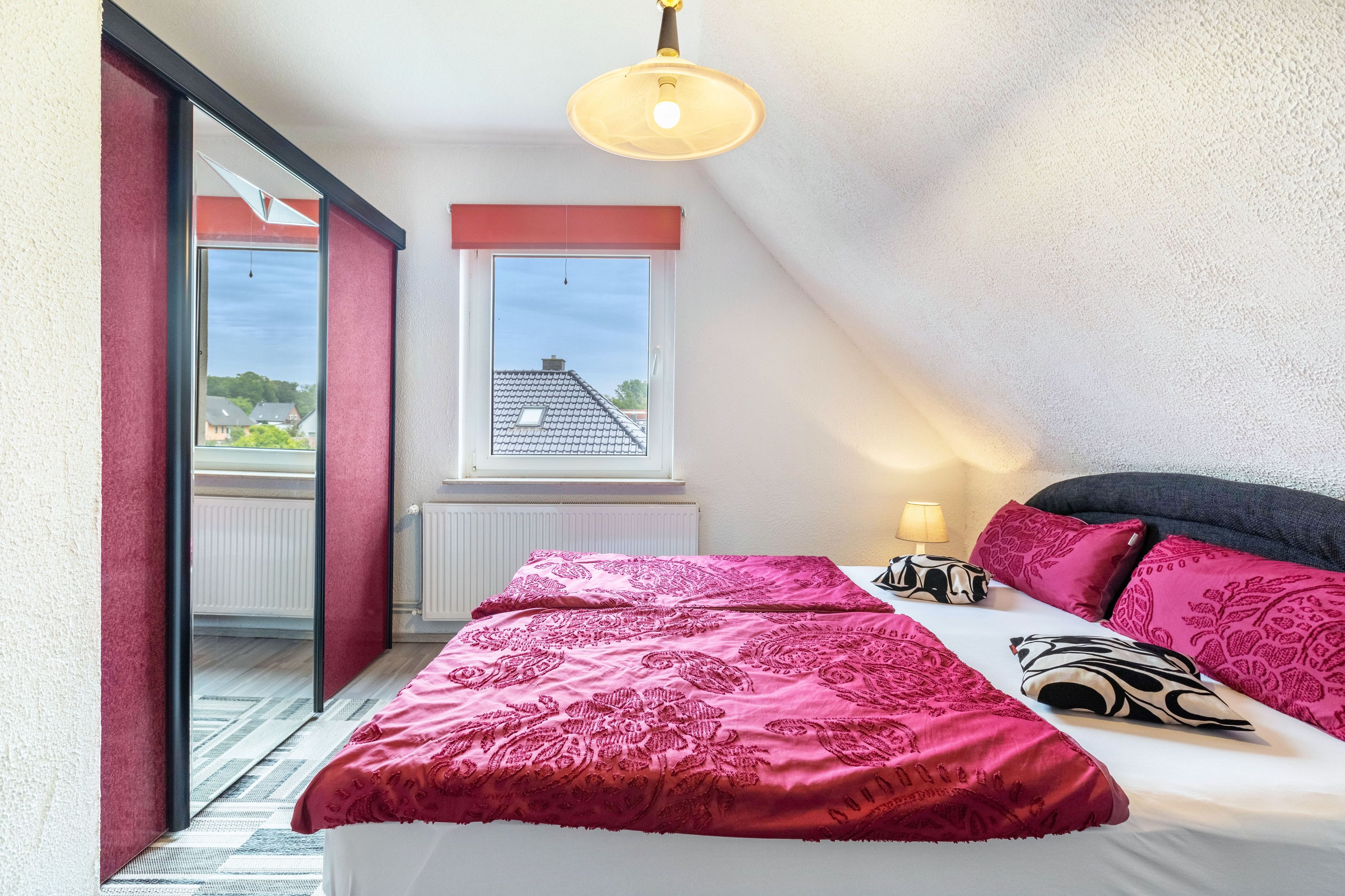 Une chambre avec un grand lit, une fenêtre donnant sur un beau paysage et un luminaire au plafond.