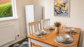 A dining area with a wooden table set for four, white chairs, and a white refrigerator in the background.