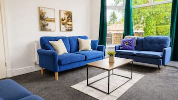 A living room with two blue sofas, a coffee table, and a view of greenery outside.