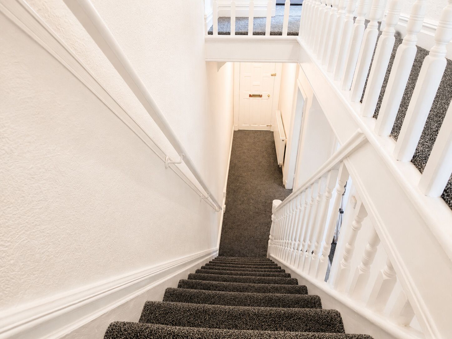 A staircase with white railings and carpeted steps leading to a door at the top.