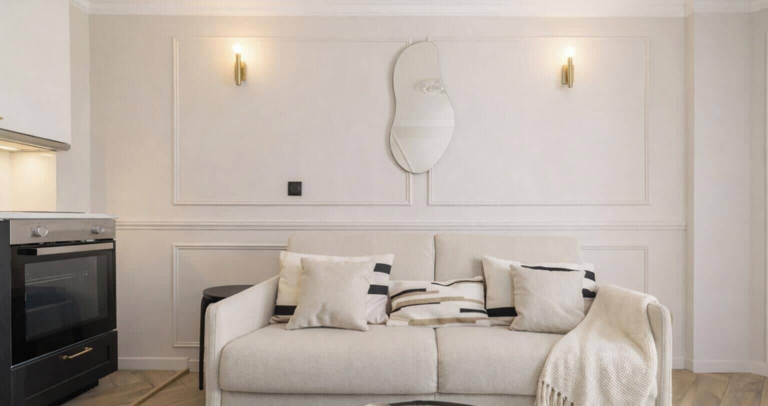 Una sala de estar con un sofá, un espejo decorativo e iluminación en la pared.