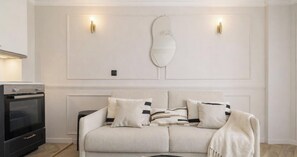 Un salon comprenant un canapé, un miroir décoratif et des luminaires fixés au mur.