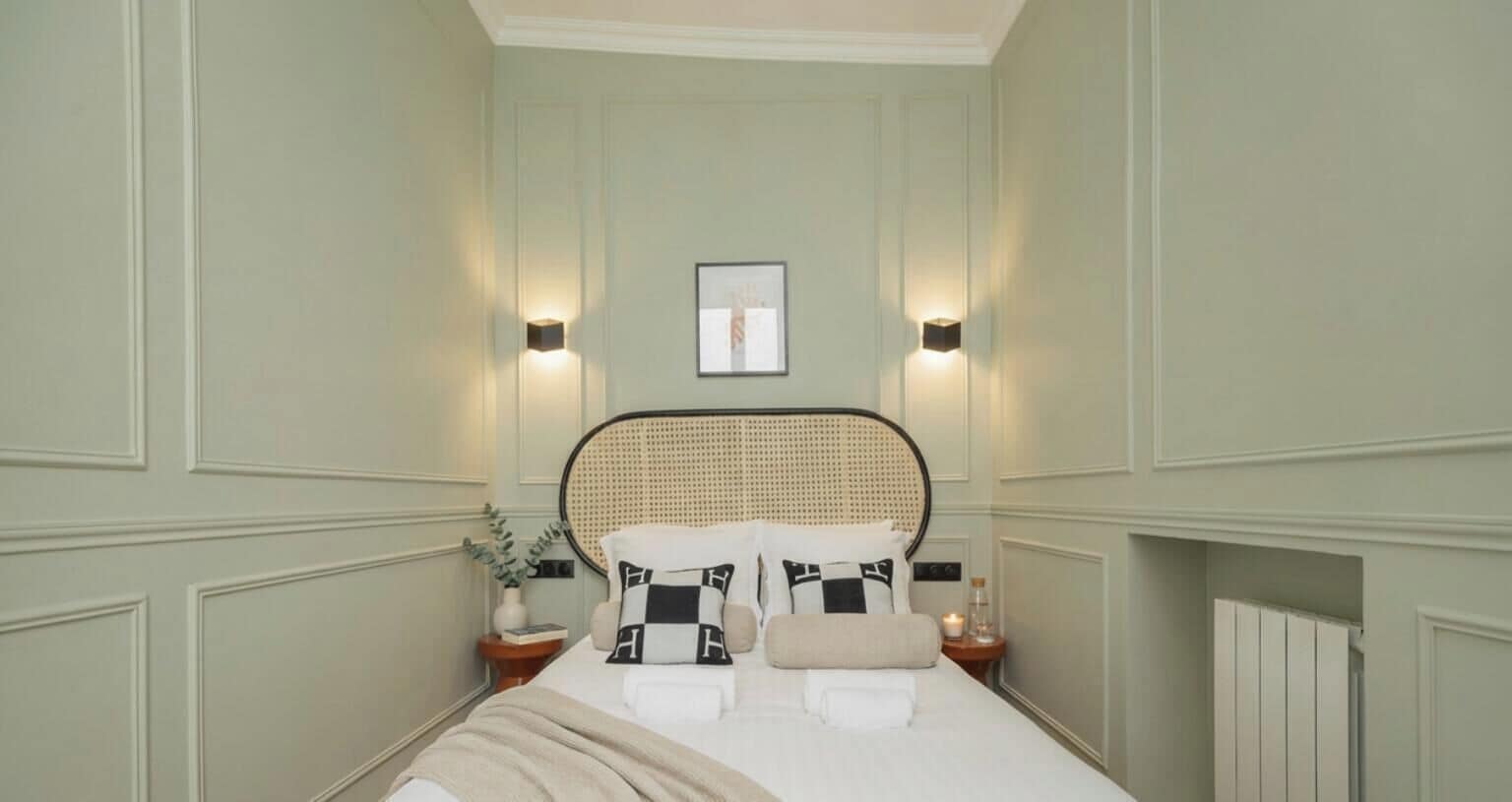 A neatly arranged bedroom with a bed, two bedside tables, a wall-mounted light, and a framed picture.