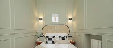 A neatly arranged bedroom with a bed, two bedside tables, a wall-mounted light, and a framed picture.