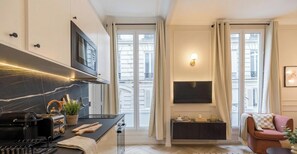 A modern kitchen with a built-in oven, a microwave, and a stove. There is a dining area with a table and chairs, and a large window with curtains. - PoeticStay - Opéra - Hanovre (Paris)