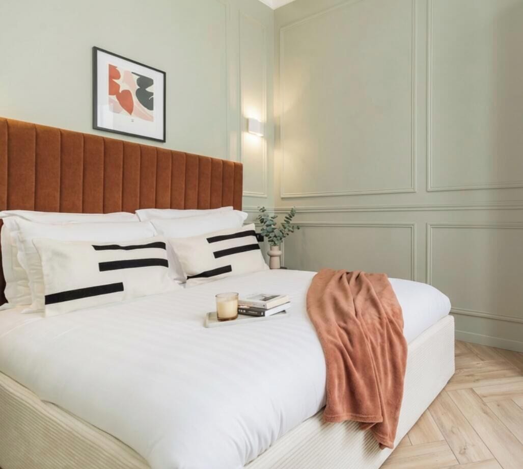 A neatly made bed with a brown headboard, white bedding, and a single brown throw blanket.