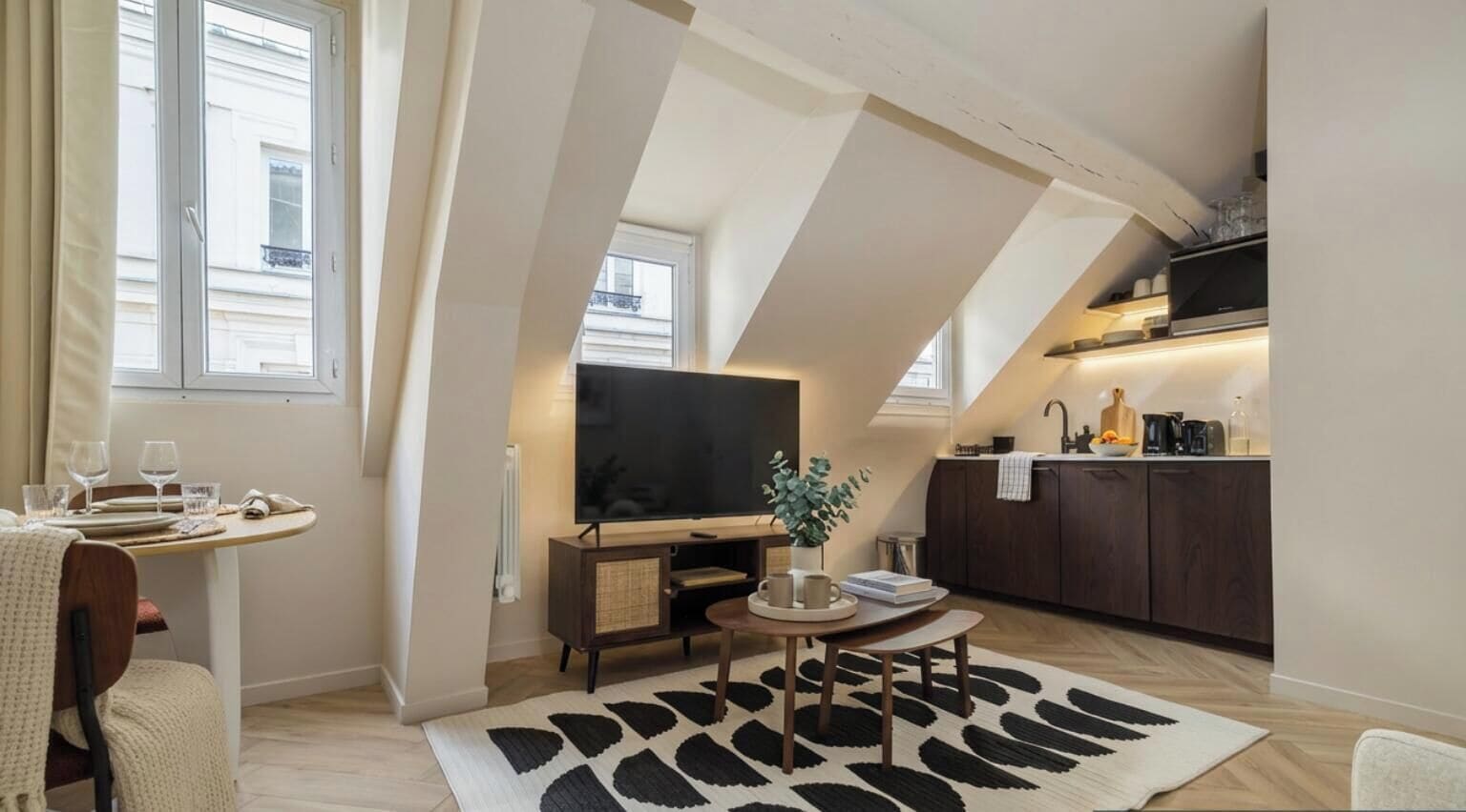 Un espacio habitable compacto con zona de comedor, televisor de pantalla plana, cocina equipada con cafetera y un ventanal grande.