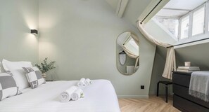 A bedroom with a bed, a bedside table, a mirror, and a window with curtains. - PoeticStay - Opéra - Hanovre (Paris)
