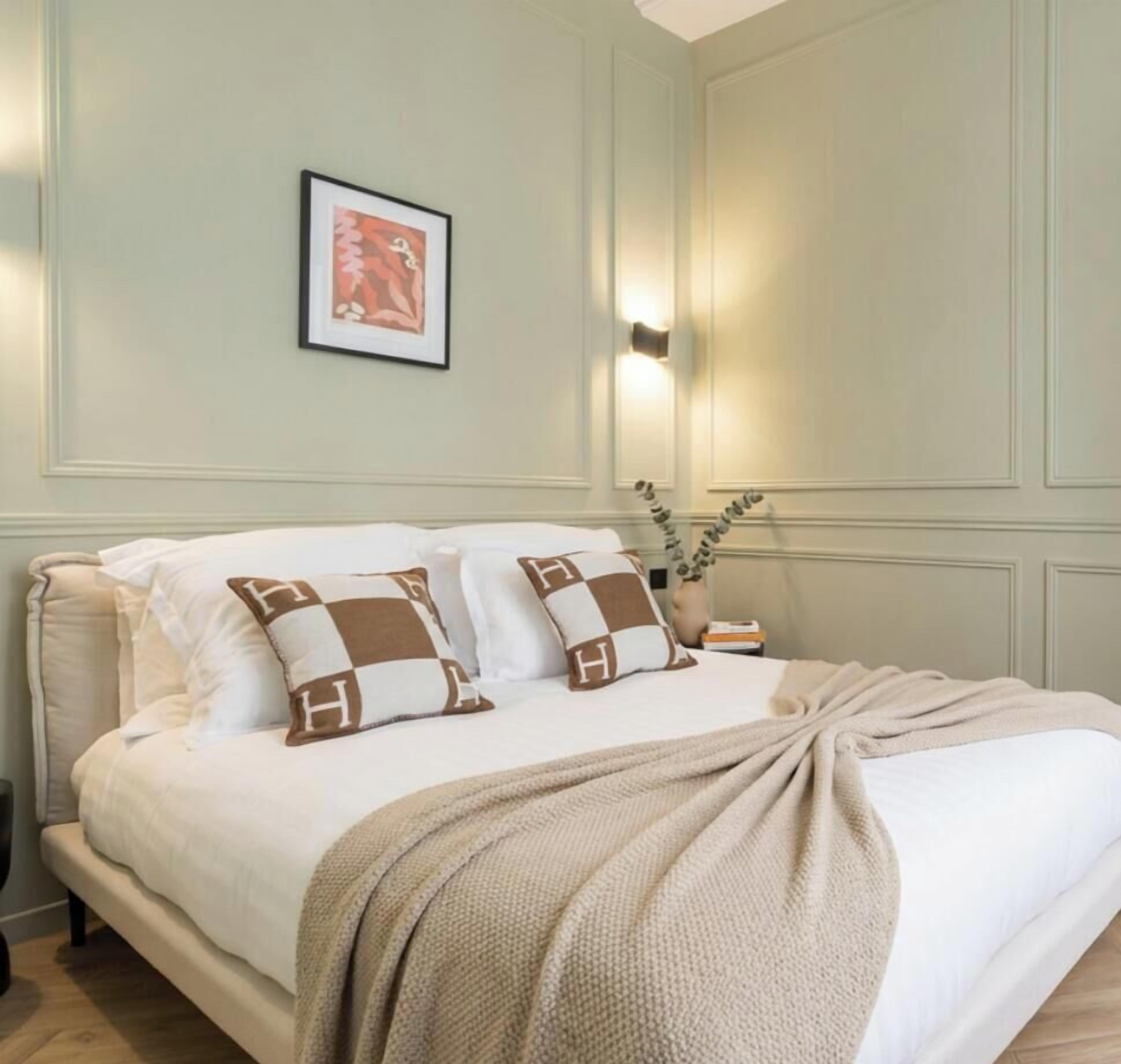 Una cama bien hecha con un diseño de almohada a cuadros, una mesita de noche con lámpara y un cuadro enmarcado en la pared.
