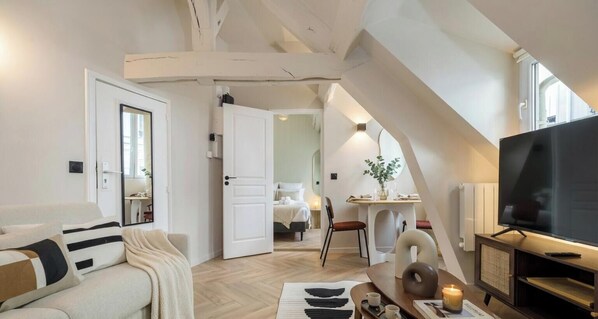 A modern interior with a sofa, a dining area, a TV, and a bedroom visible through an open door. - PoeticStay - Opéra - Hanovre (Paris)