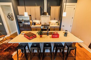 A kitchen with a central island, bar stools, a refrigerator, a stove, and a sink. - Johnny Cash's Ring of Fire Retreat: Rooftop Deck (Nashville)