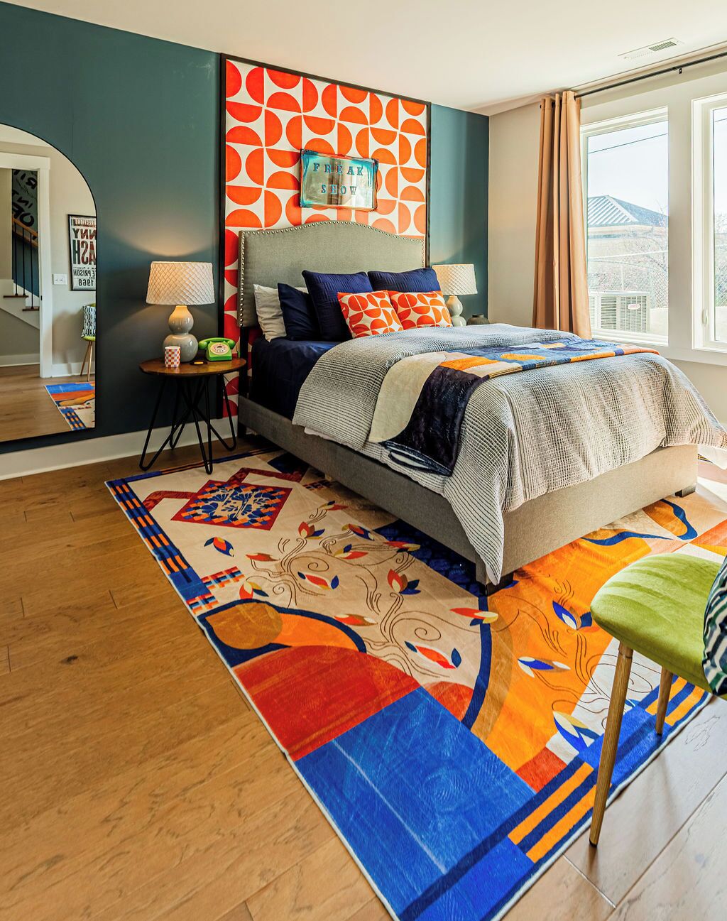 Un dormitorio con cama, mesita de noche, lámpara, ventana con cortinas y una alfombra colorida.