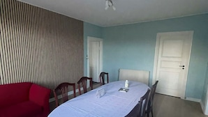 Ein Essbereich mit einem Tisch für vier Personen, umgeben von Holzsesseln, einem roten Sofa und einer gestreiften Wand.