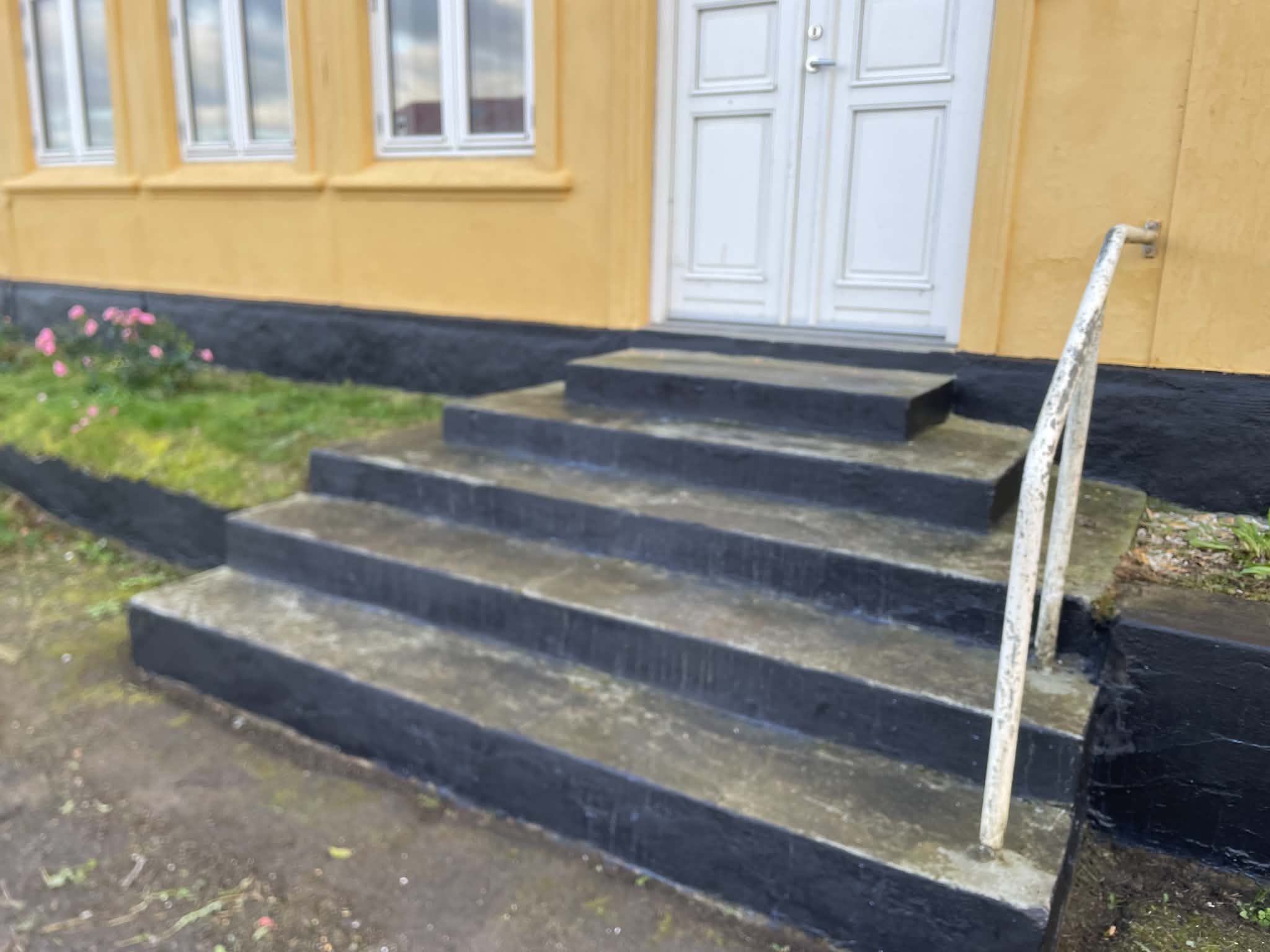 A set of concrete steps leading to a white door, with a handrail on the right.
