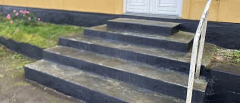 Una serie de escalones de hormigón que conducen a una puerta blanca, con un pasamanos a la derecha.