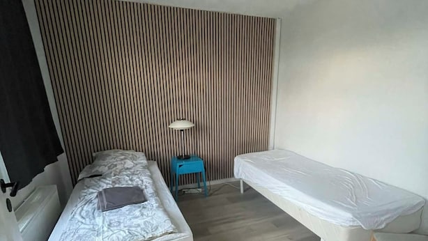 Ein Zimmer mit einem Bett, einem kleinen Tisch, einem Stuhl und einem Fenster mit Jalousien.