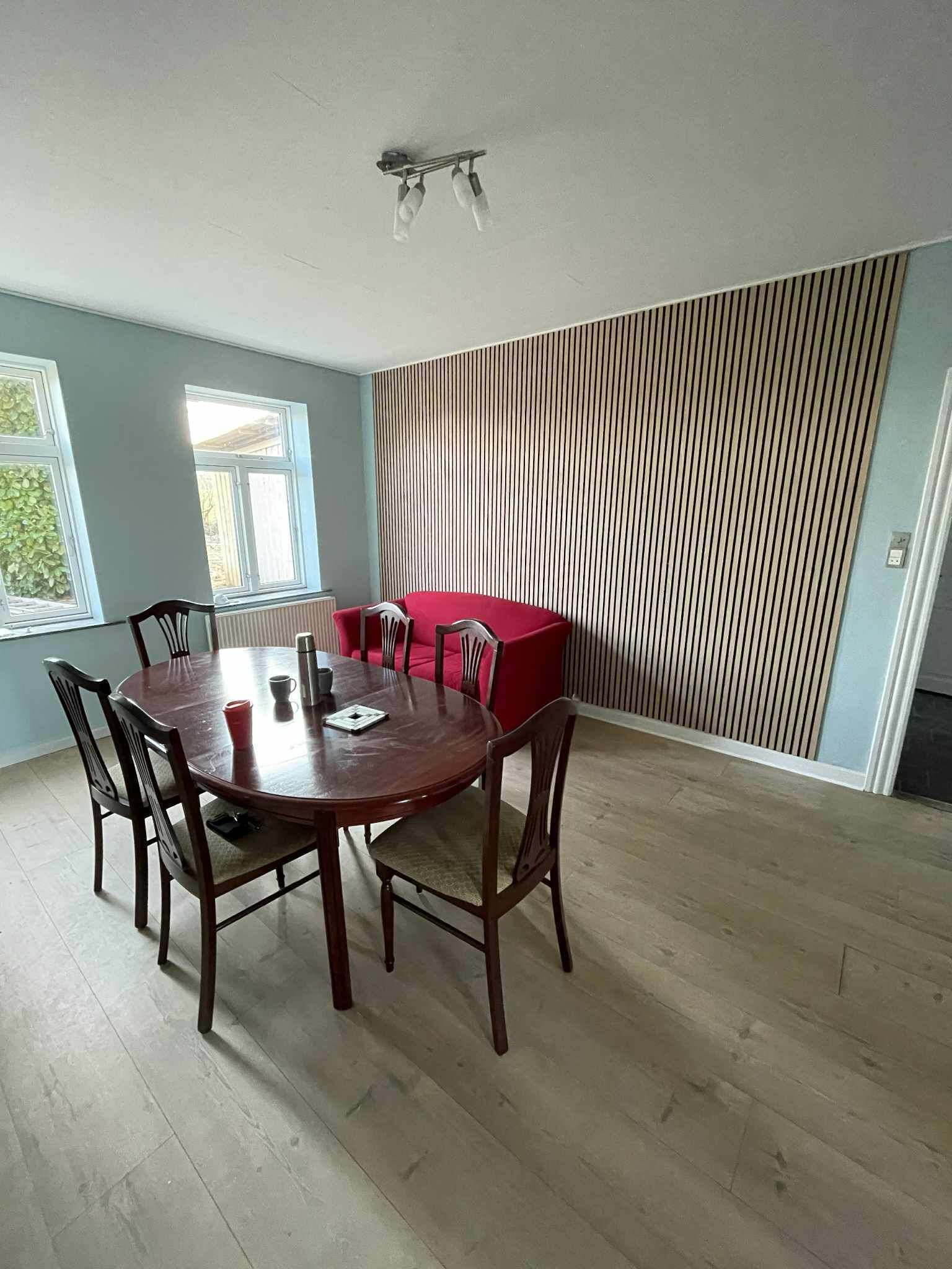 Et spiseområde med et rundt bord, seks stole og en rød sofa.
