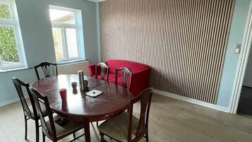 Et spiseområde med et rundt bord, seks stole og en rød sofa.