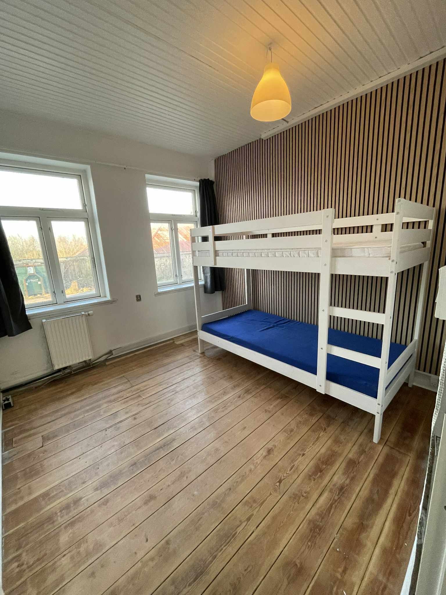 A room with a bunk bed, wooden flooring, a radiator, and a window.