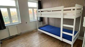 A room with a bunk bed, wooden flooring, a radiator, and a window.