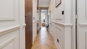 Un pasillo con paredes blancas y puertas de madera, que conduce a una habitación con una cama y una planta.