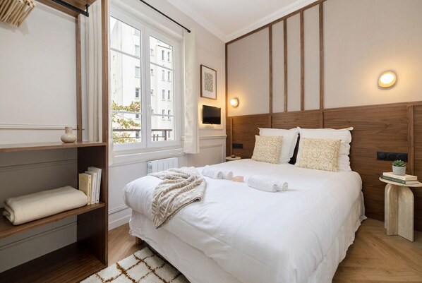Habitación de hotel con una cama grande, una mesita de noche, un televisor y una ventana con vista a edificios.